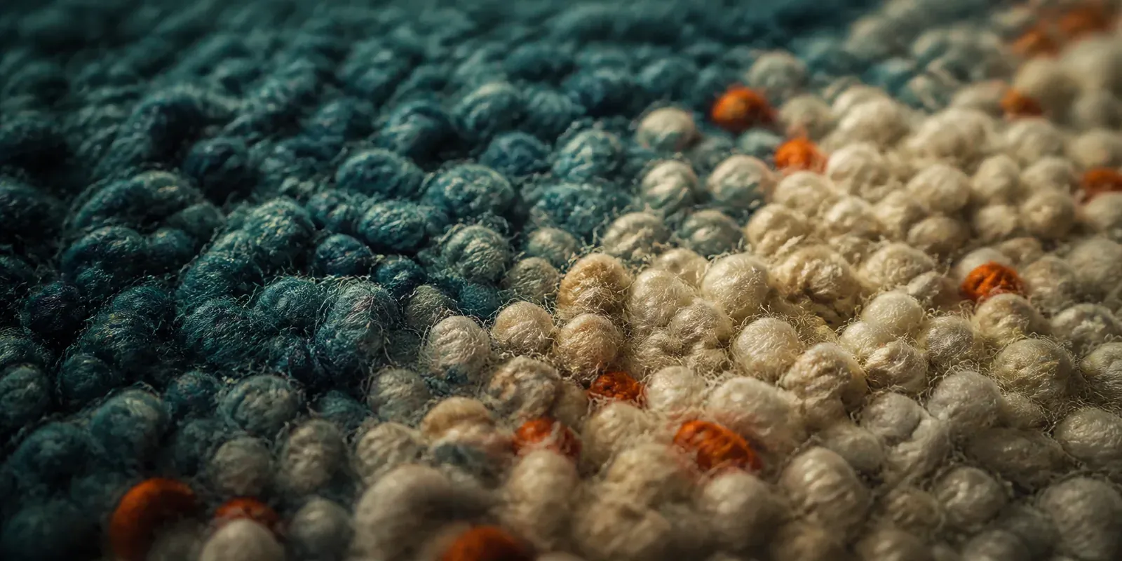 Gros plan sur le velours d'un tapis tufté : boucles de laine épaisse bleu canard, crème et orange